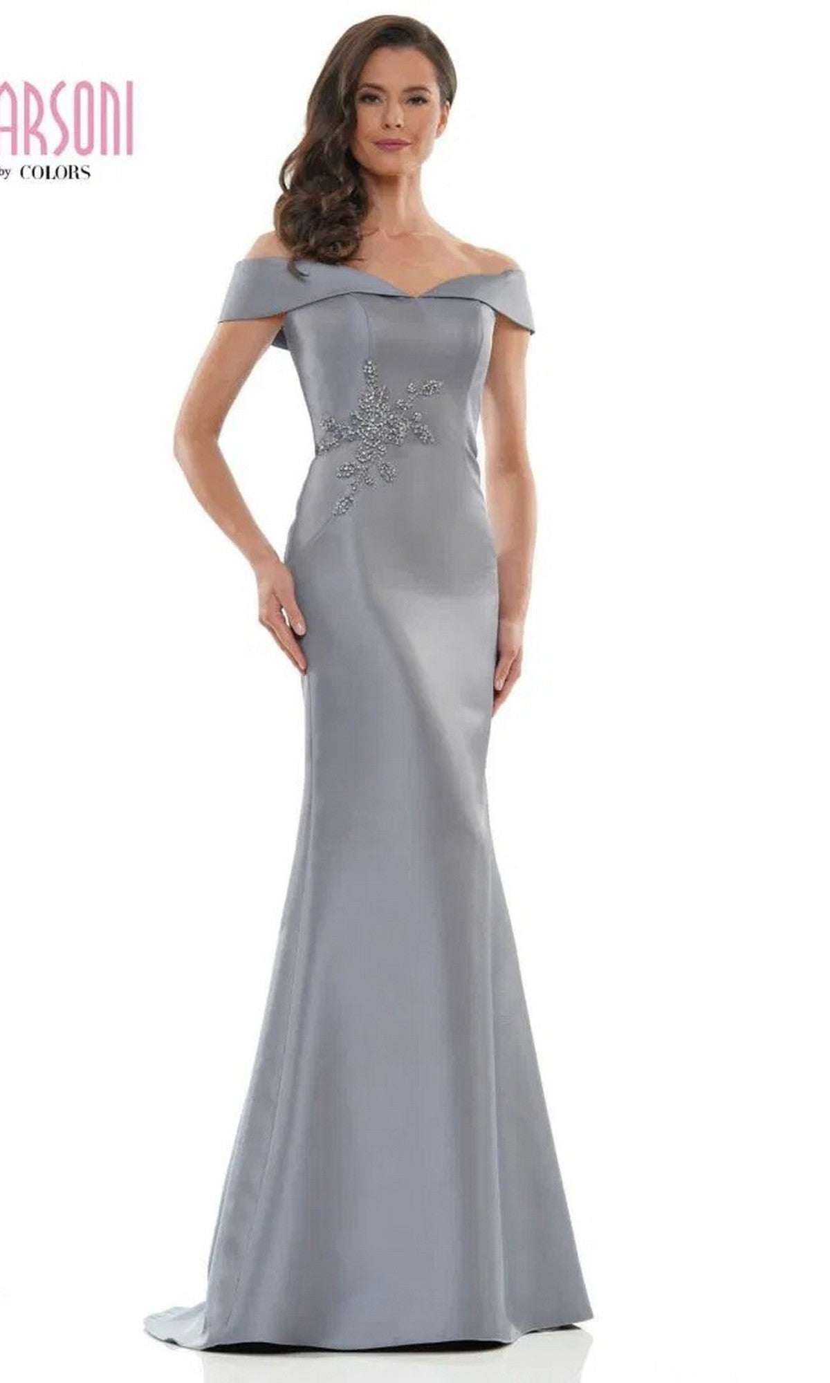 A woman models the Marsoni MV1003 long formal dress, a floor-length off-the-shoulder satin gown with beaded floral waist embellishment, standing against a plain white background.